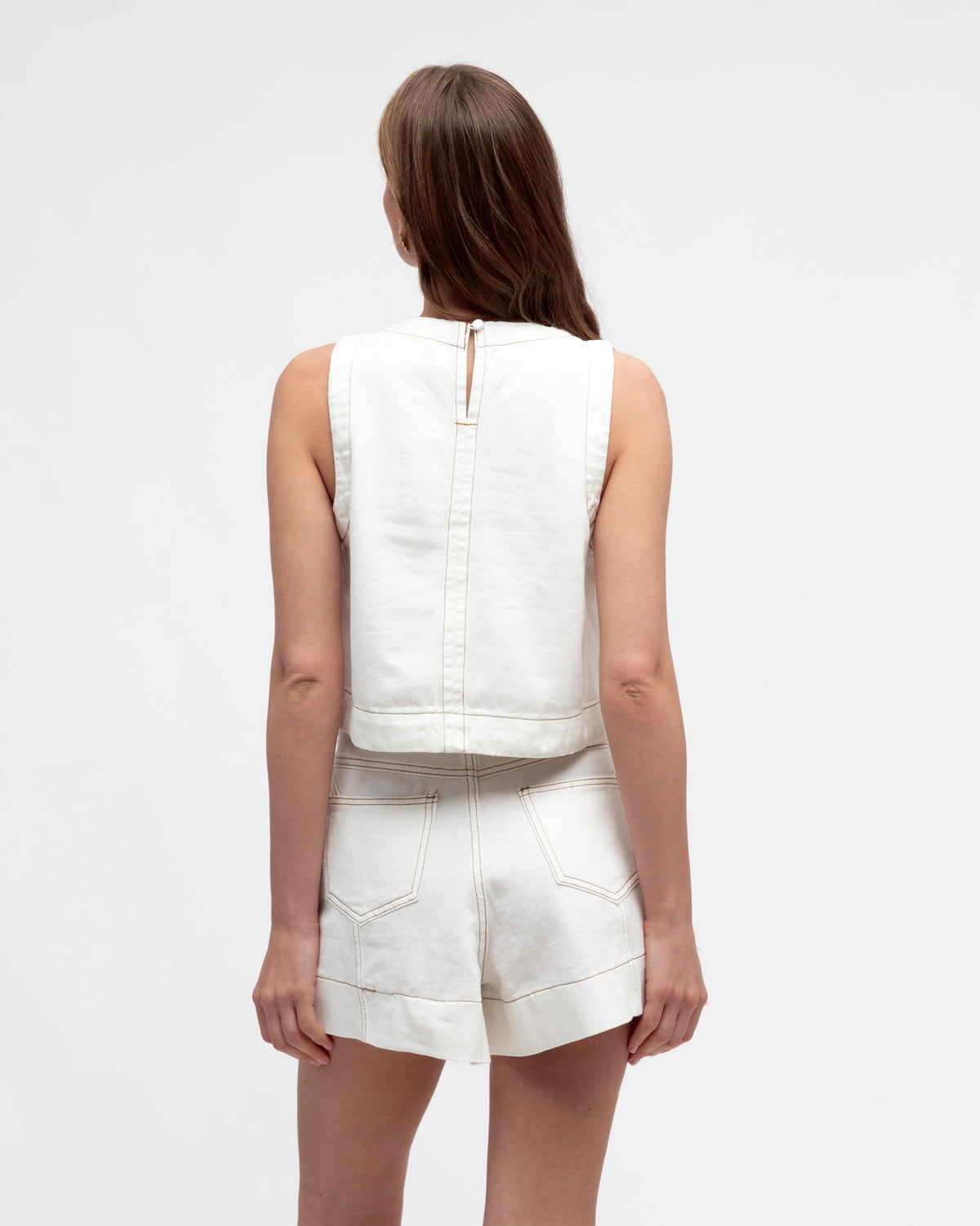 Woman wearing a white sleeveless top and shorts set on a plain background