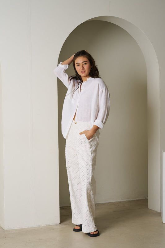 Woman in a white outfit standing in an archway with a neutral background